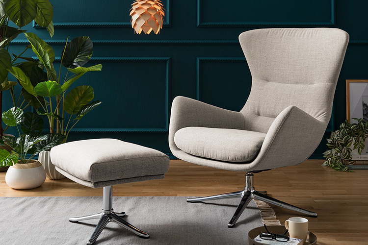 Fauteuil de relaxation gris clair Hepburn par Studio Copenhagen et repose-pieds coordonné, devant un mur bleu foncé.