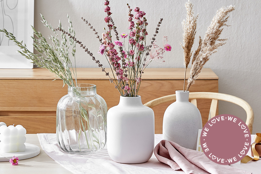 Heller Holztisch mit drei Trockenblumensträußen in großen Vasen arrangiert