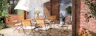 Terrasse mit Gartentisch, Gartenstühlen und Gartenbank aus Akazienholz mit hellblauen Sitzkissen, dazu ein weißer Sonnenschirm, ein gemusterter Outdoor-Teppich und Deko.