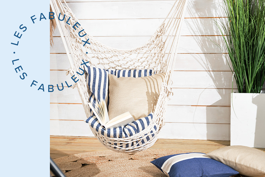 Fauteuil suspendu blanc avec coussin d'assise rayé bleu et blanc et coussins beiges devant  un mur en bois