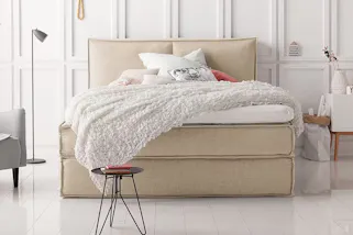 Beiges Boxspringbett KINX mit weißer Bettwäsche.