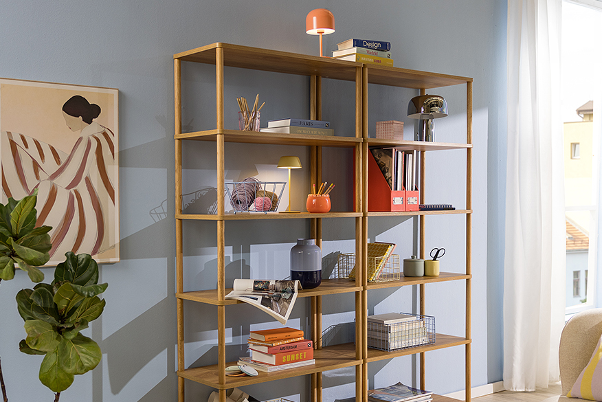 Modernes Standregal aus Holz vor himmelblauer Wand, dekoriert mit Körben, Büchern und Deko, dazu ein Holzregal mit Büchern und Schreibartikeln.
