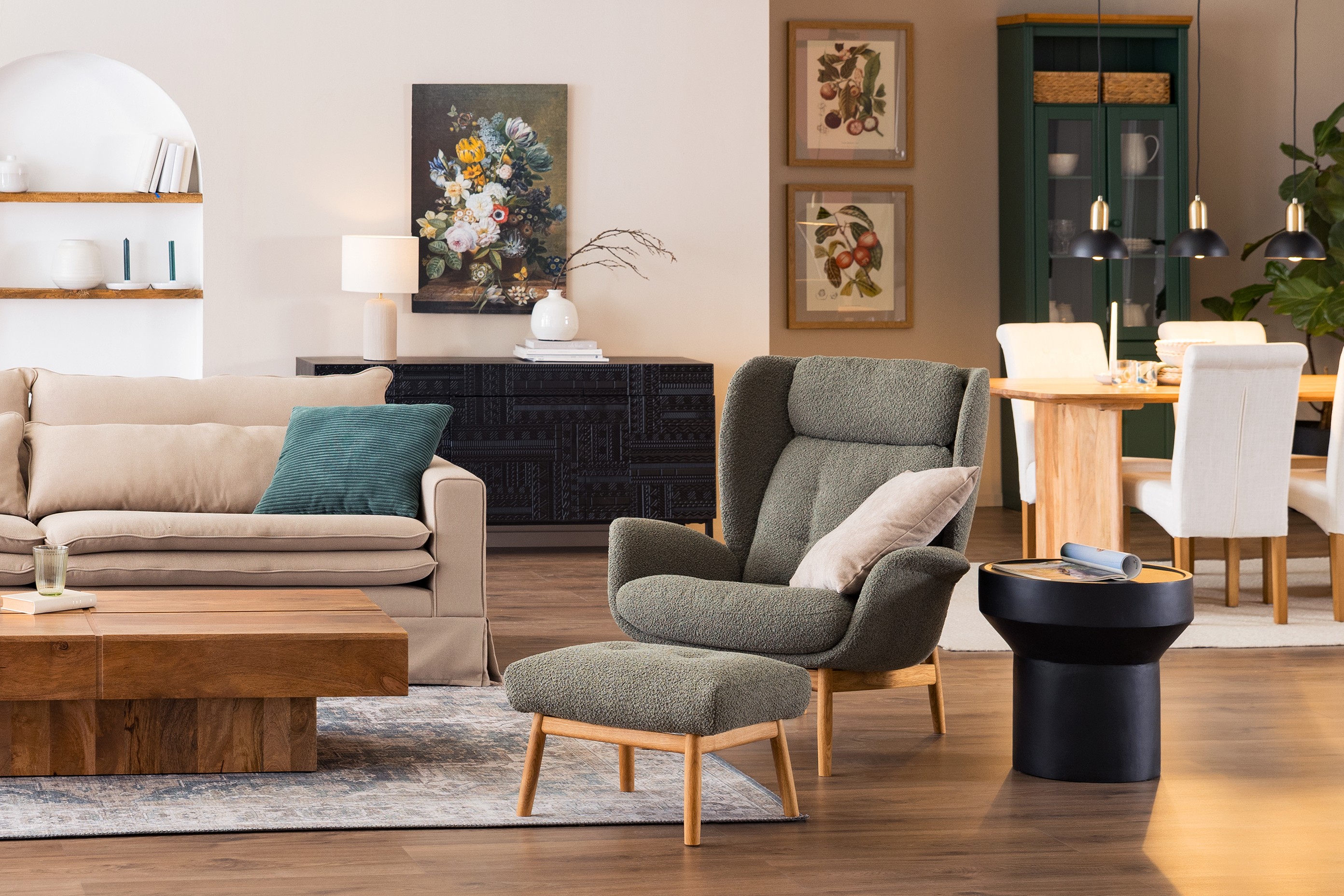 Offener Wohn- und Essbereich im britischen Landhausstil mit einem Couchtisch aus massivem Holz, einem beigen Sofa, einem moosgrünen Ohrensessel, vielen Textilien und einem stilvollen Tassenregal.