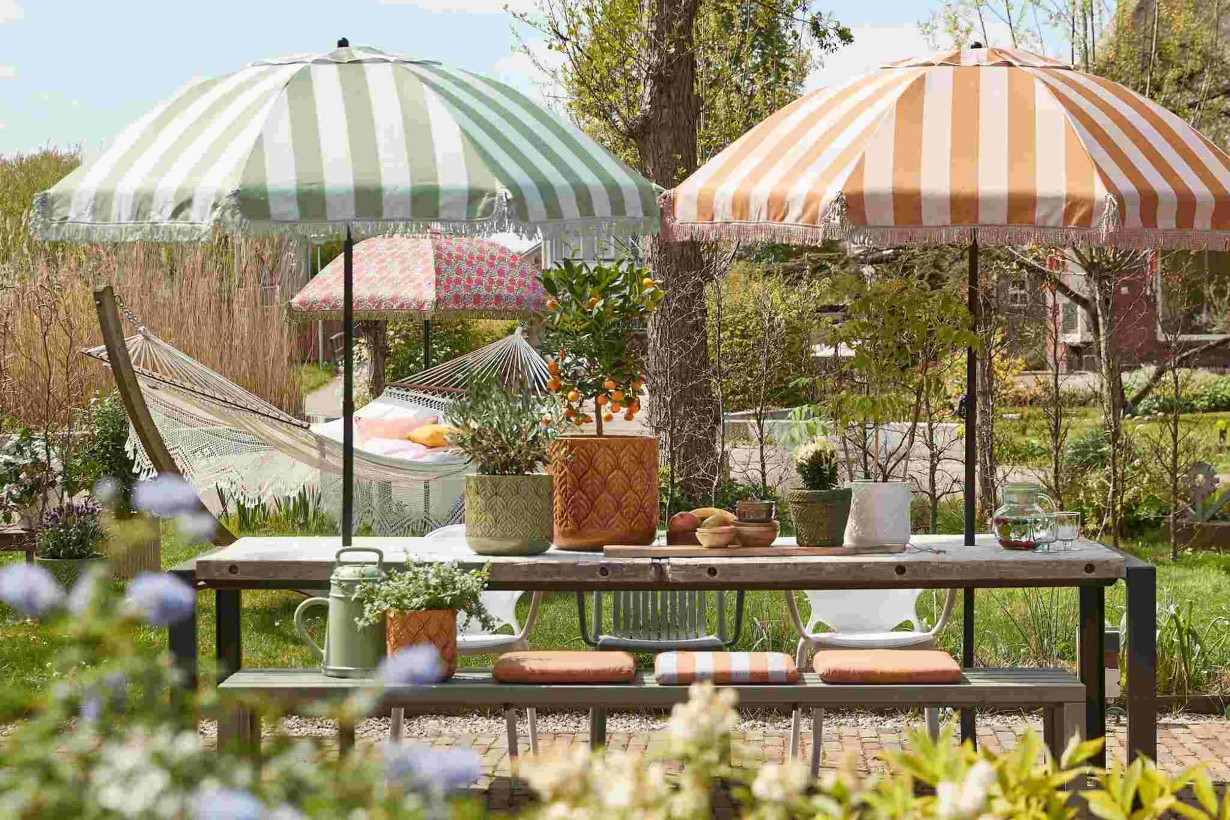 Grüner Garten mit zwei gestreiften Sonnenschirmen, Sitzecke und Hängematte