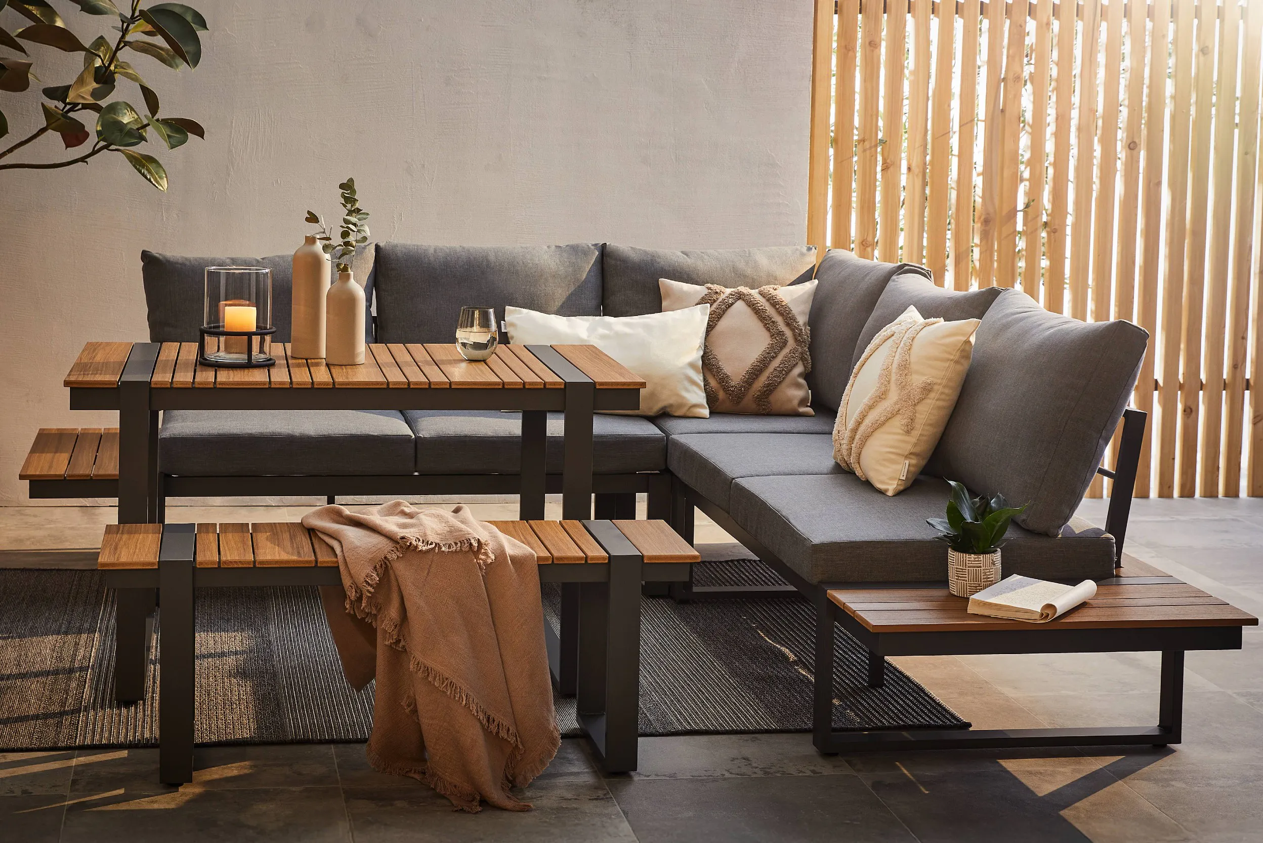 Gartensitzgruppe mit grau gepolstertem Ecksofa, Tisch und Bank, sowie Dekokissen und Accessoires