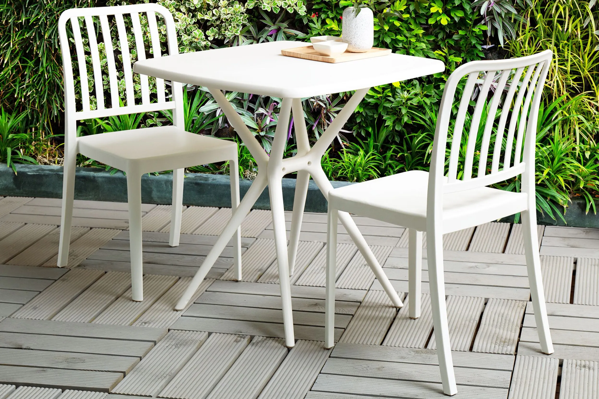 Weisser Tisch mit passenden Stühlen auf einer Terrasse im Grünen