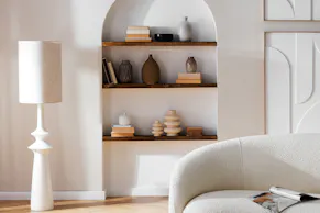 Canapé Osane crème au design organique moderne, lampadaire blanc ainsi que des décorations en céramique et en bois dans des tons terre.