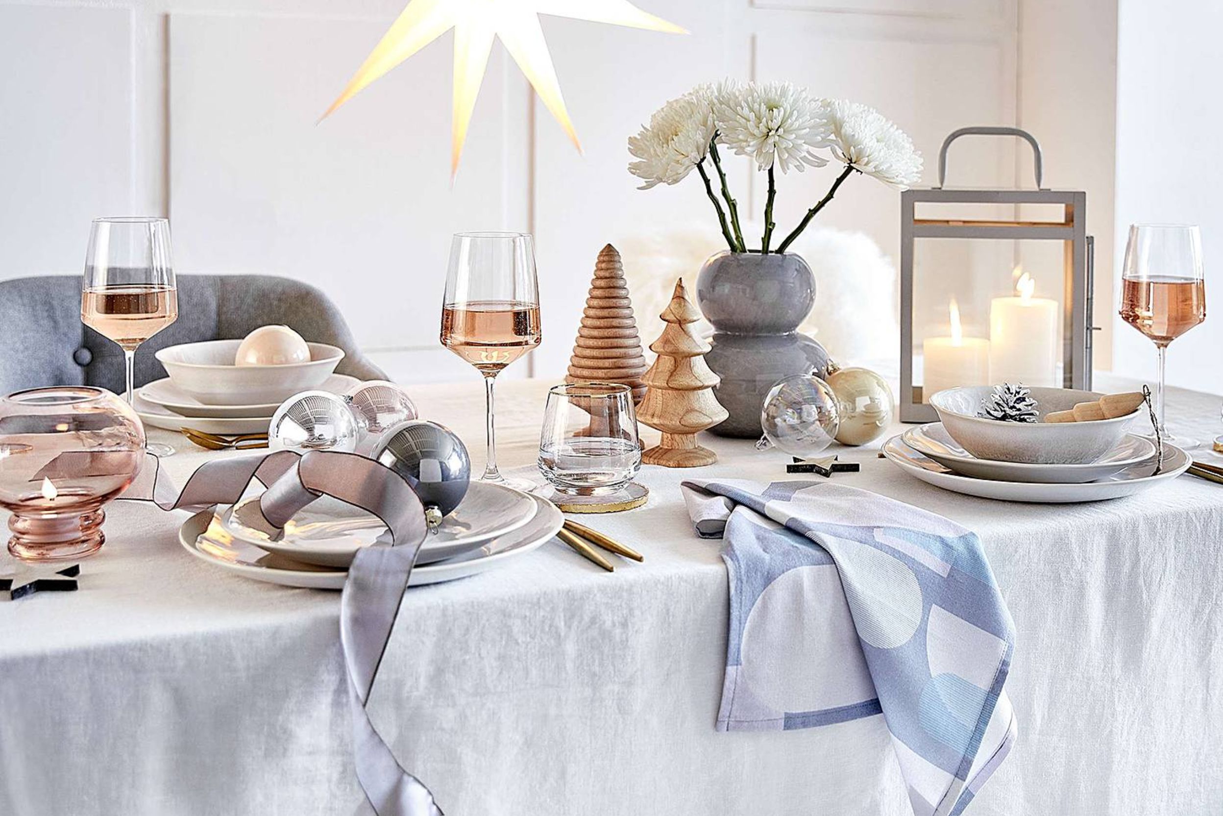 Ein raffiniertes, minimalistisches Arrangement von home24 für die Feiertage. Der Tisch ist mit einer Leinentischdecke und Geschirr mit klaren Linien geschmückt. Sanfte, natürliche Farben wie Weiß, Grau und Puderrosa schaffen eine ruhige und anspruchsvolle Atmosphäre. Holz- und Metallelemente sorgen für eine warme und elegante Note.
