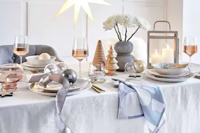 Ein raffiniertes, minimalistisches Arrangement von home24 für die Feiertage. Der Tisch ist mit einer Leinentischdecke und Geschirr mit klaren Linien geschmückt. Sanfte, natürliche Farben wie Weiß, Grau und Puderrosa schaffen eine ruhige und anspruchsvolle Atmosphäre. Holz- und Metallelemente sorgen für eine warme und elegante Note.