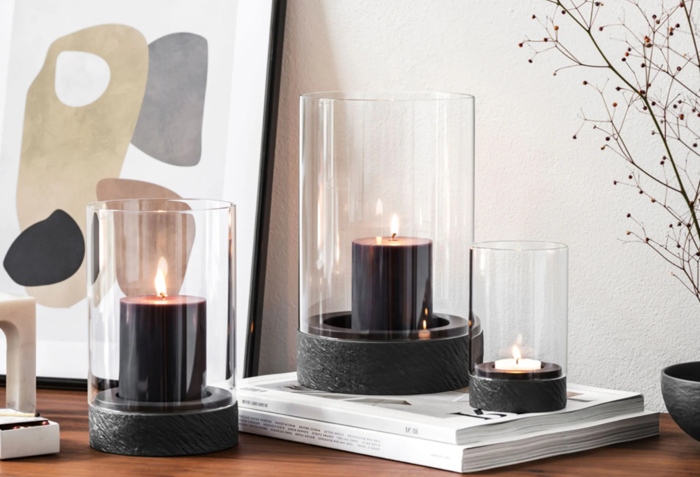Drei Windlichter auf einem Sideboard mit abstraktem Bild, Magazinen und Zweigen