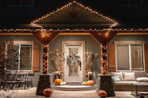 Une maison chaleureuse et accueillante illuminée par des guirlandes lumineuses, parée de décorations d'automne avec des citrouilles et des couronnes végétales, créant une atmosphère festive.