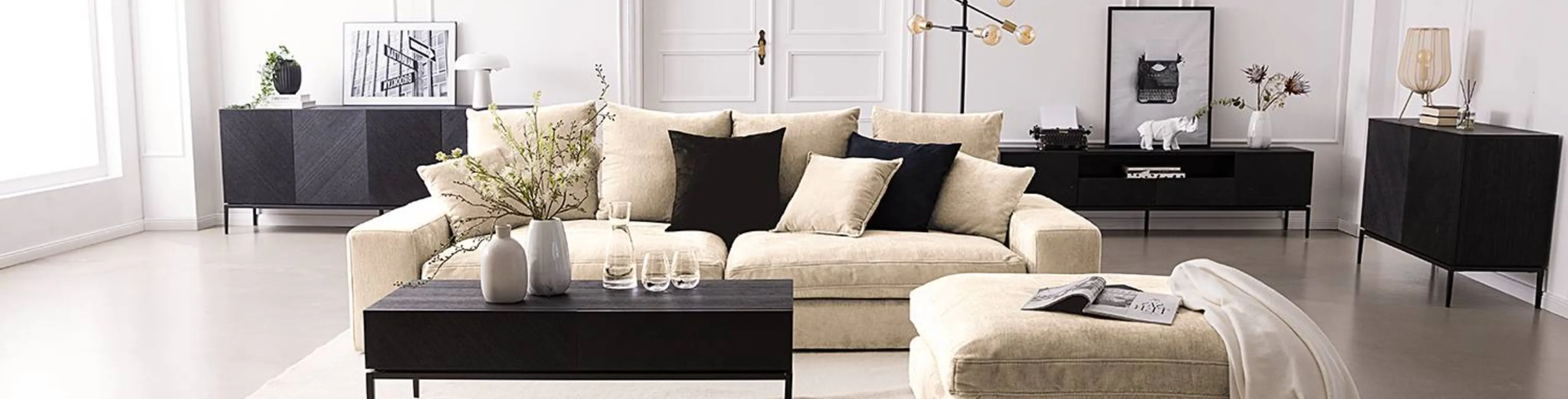 Wohnzimmer mit beiger Couch, beigem Teppich und schwarzen Möbeln