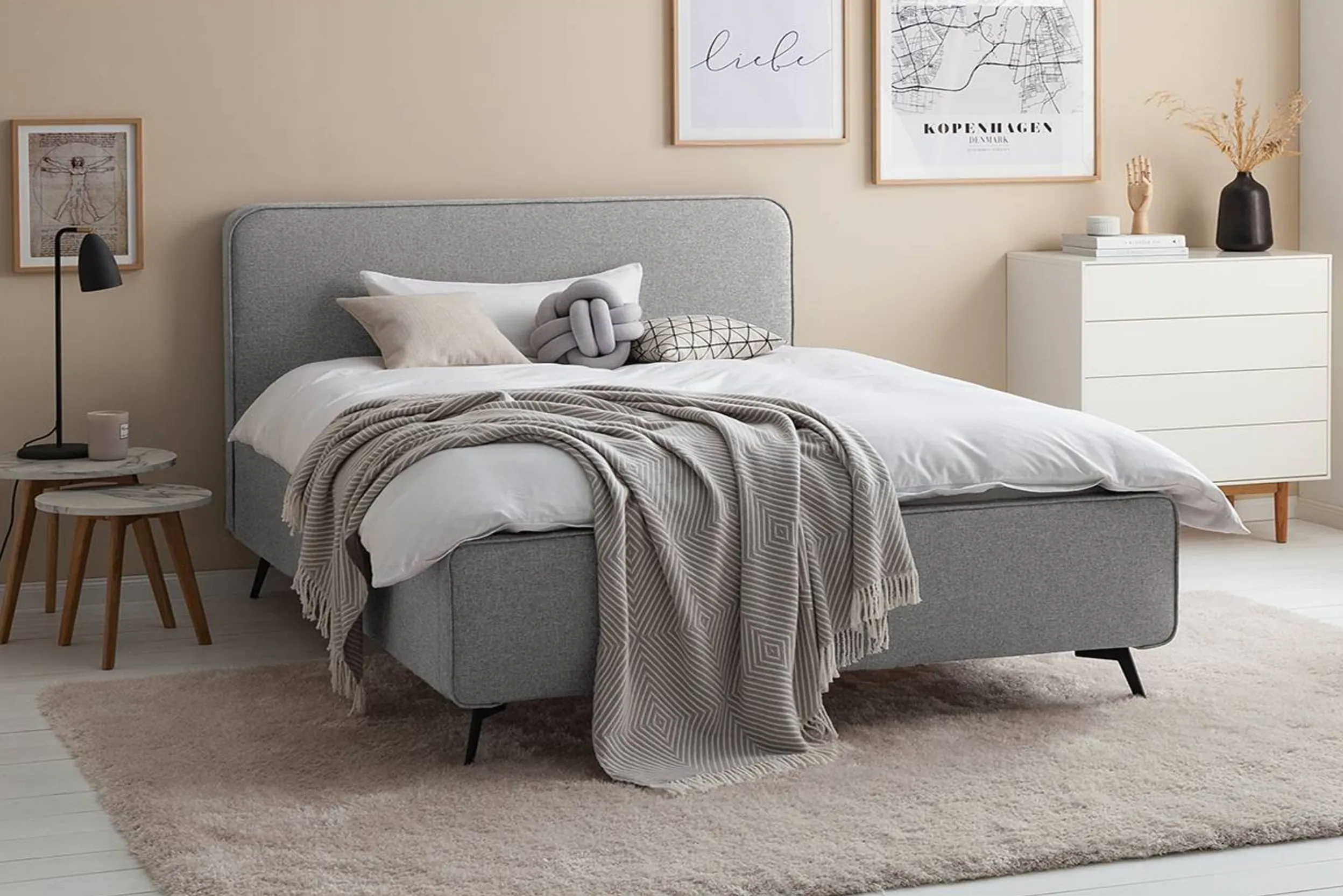 Schlafzimmer mit beiger Wand, grauem Bett und weißer Kommode