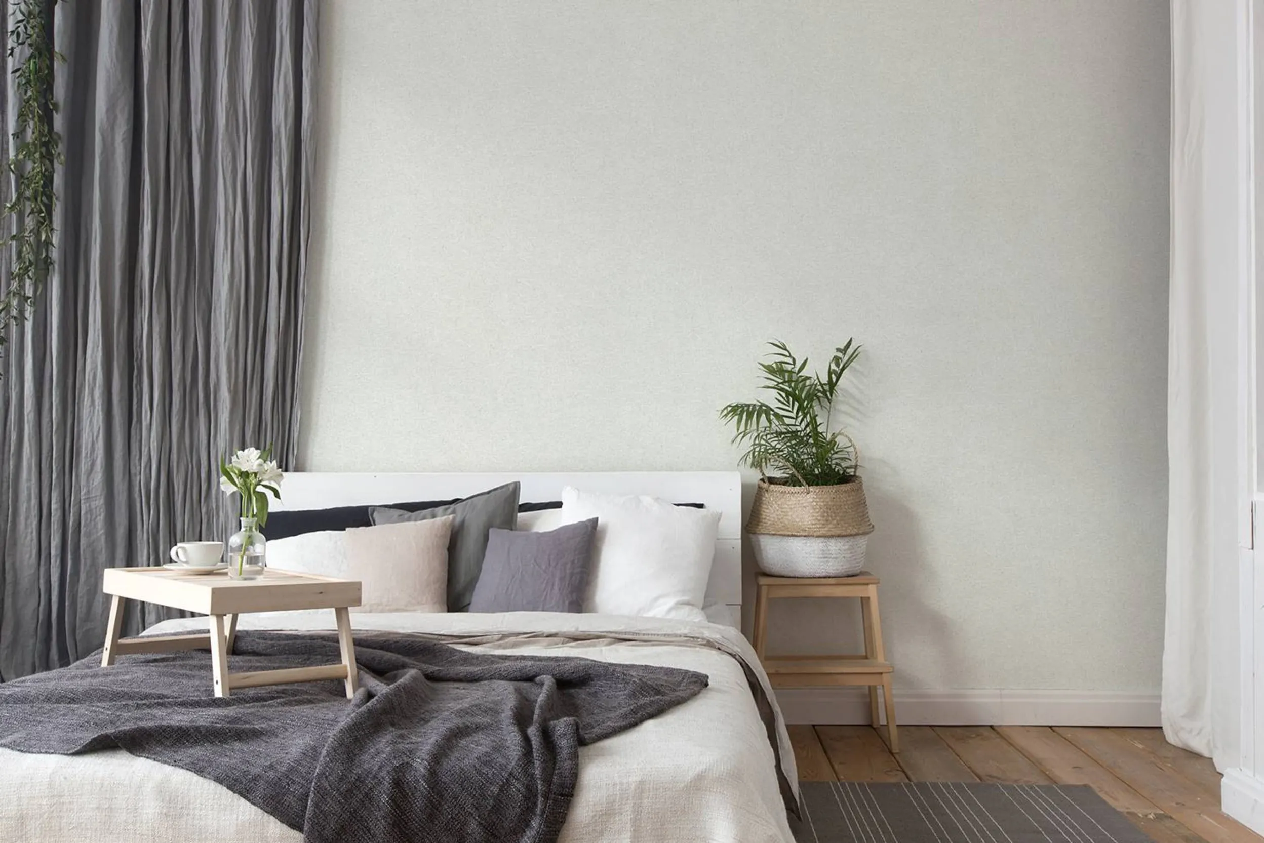 Neutrales Schlafzimmer mit grauen Textilien und einem hölzernen Nachttisch mit Pflanze