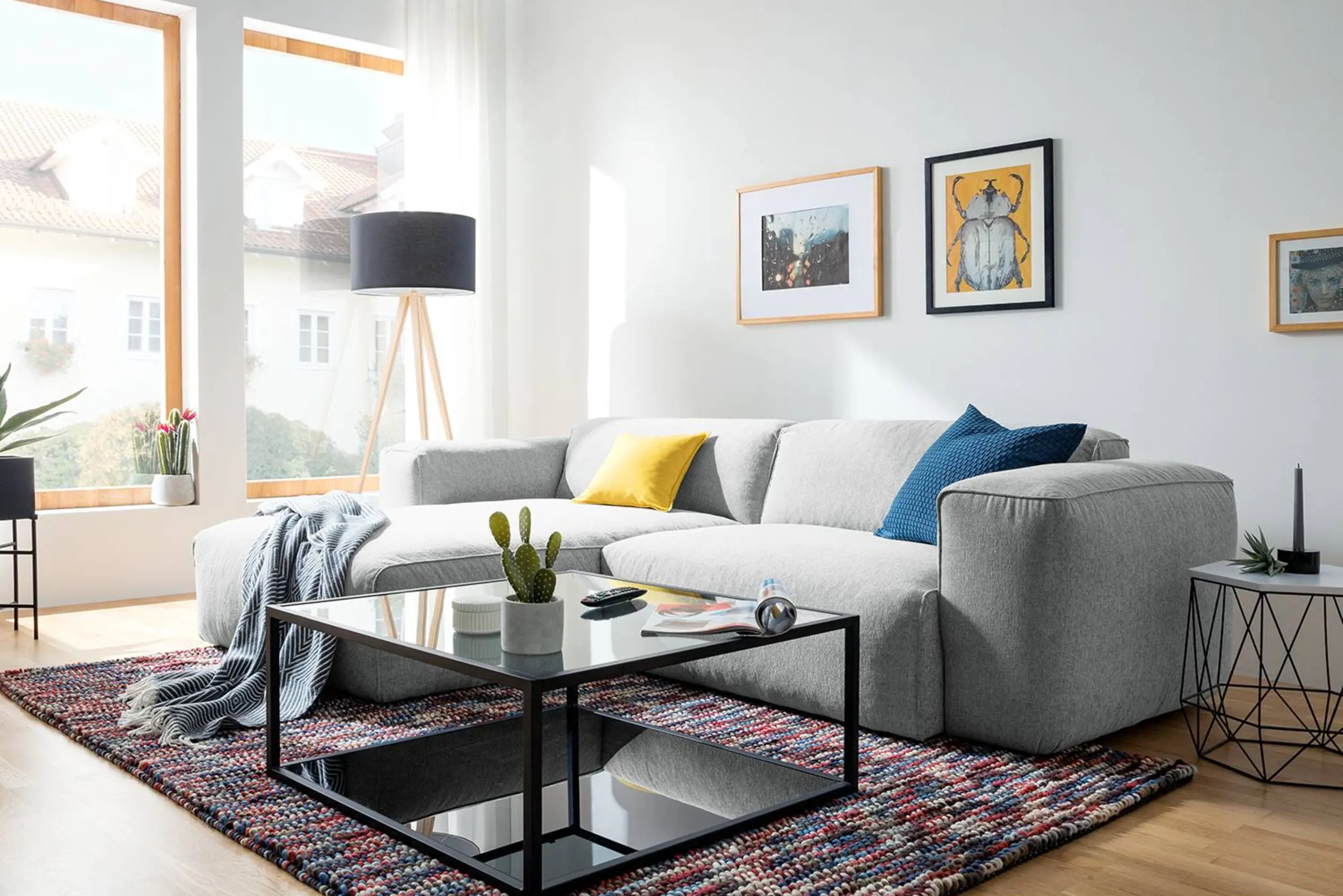 Wohnzimmer mit grauer Couch, schwarzem Couchtisch und bunten Accessoires