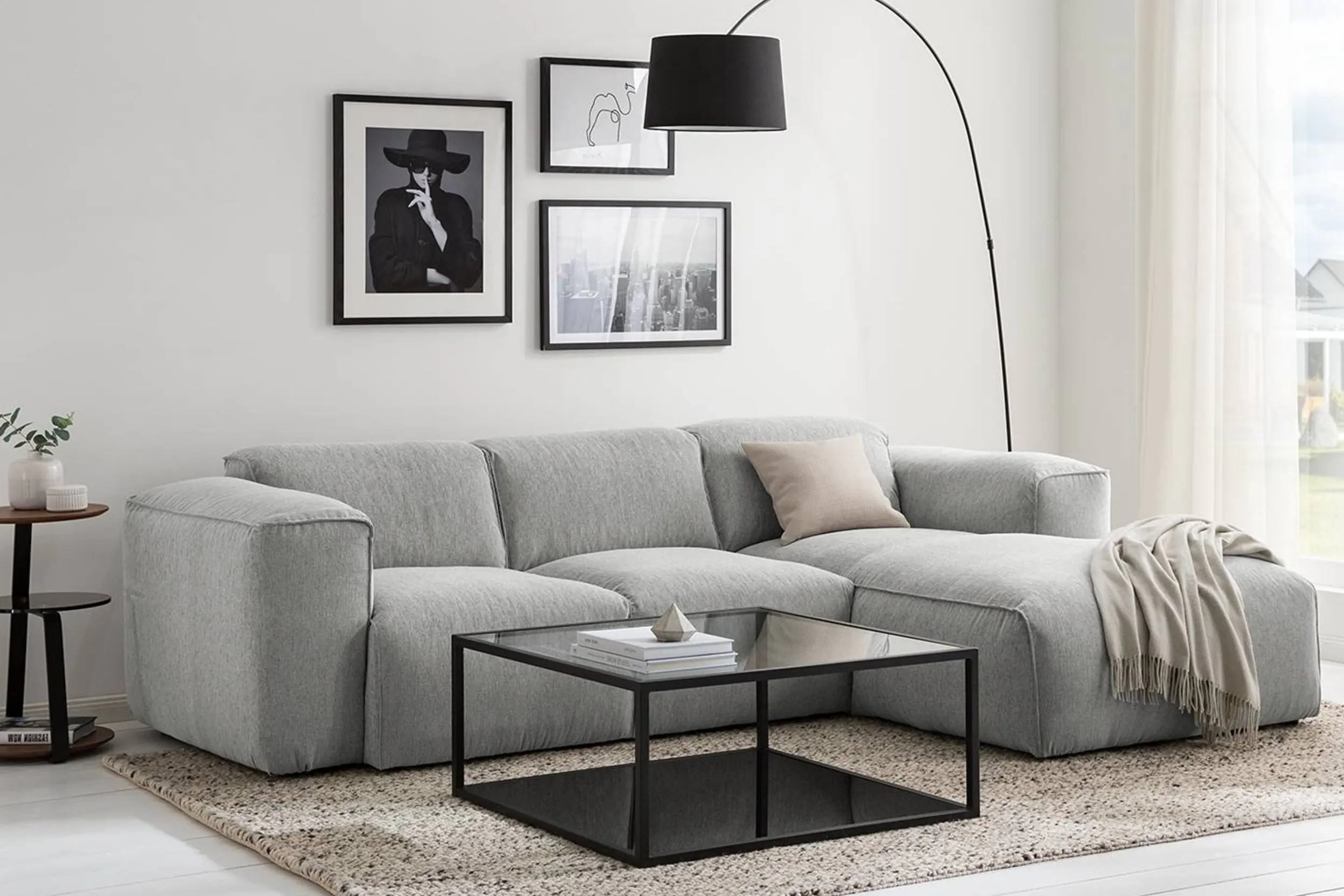 Wohnzimmer mit grauer Couch, schwarzem Glastisch und Schwarz-Weiß-Bildern