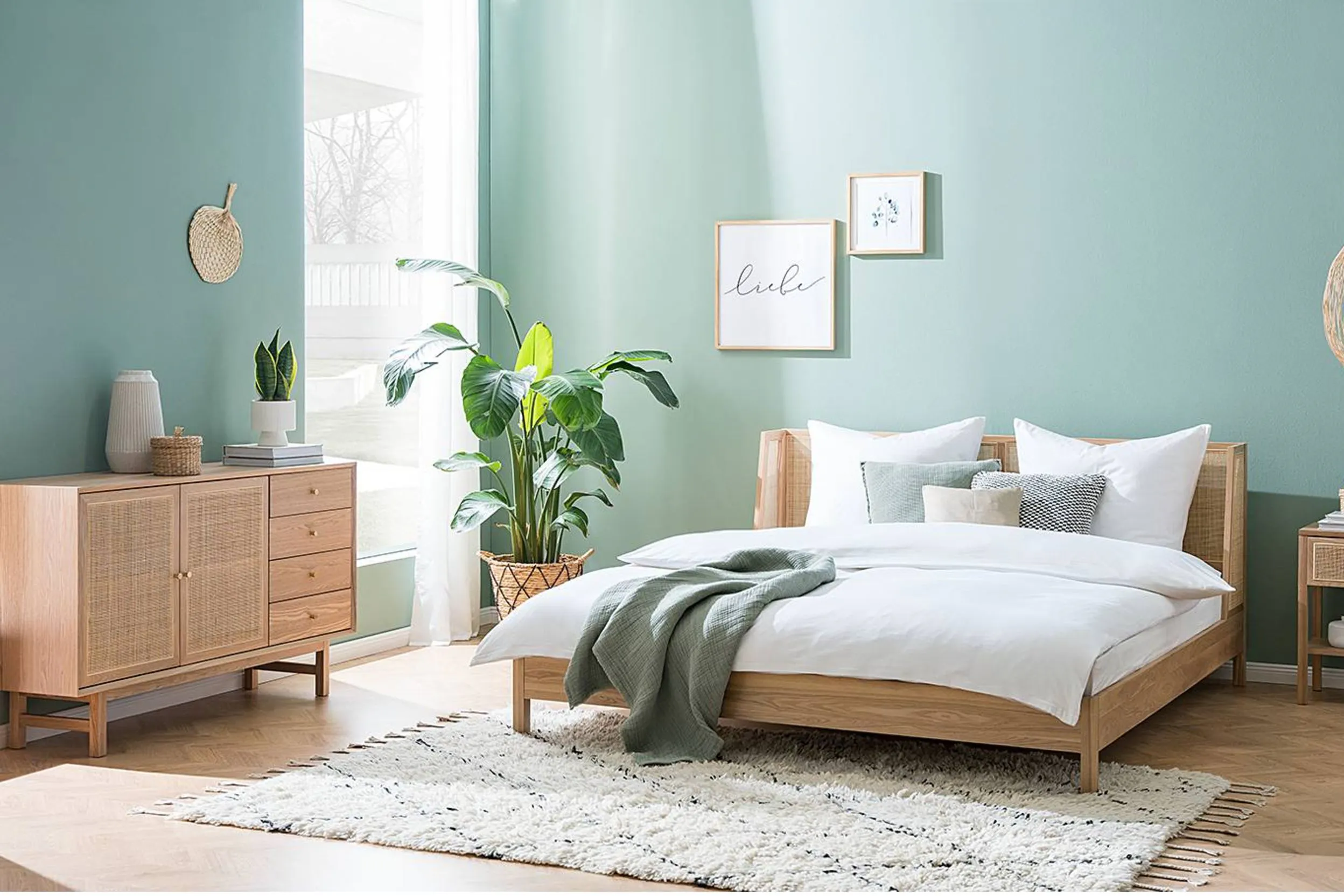 Ein Zimmer in Grüntönen mit einem Bett aus hellem Holz, weißer Bettwäsche und einem salbeigrünen Plaid