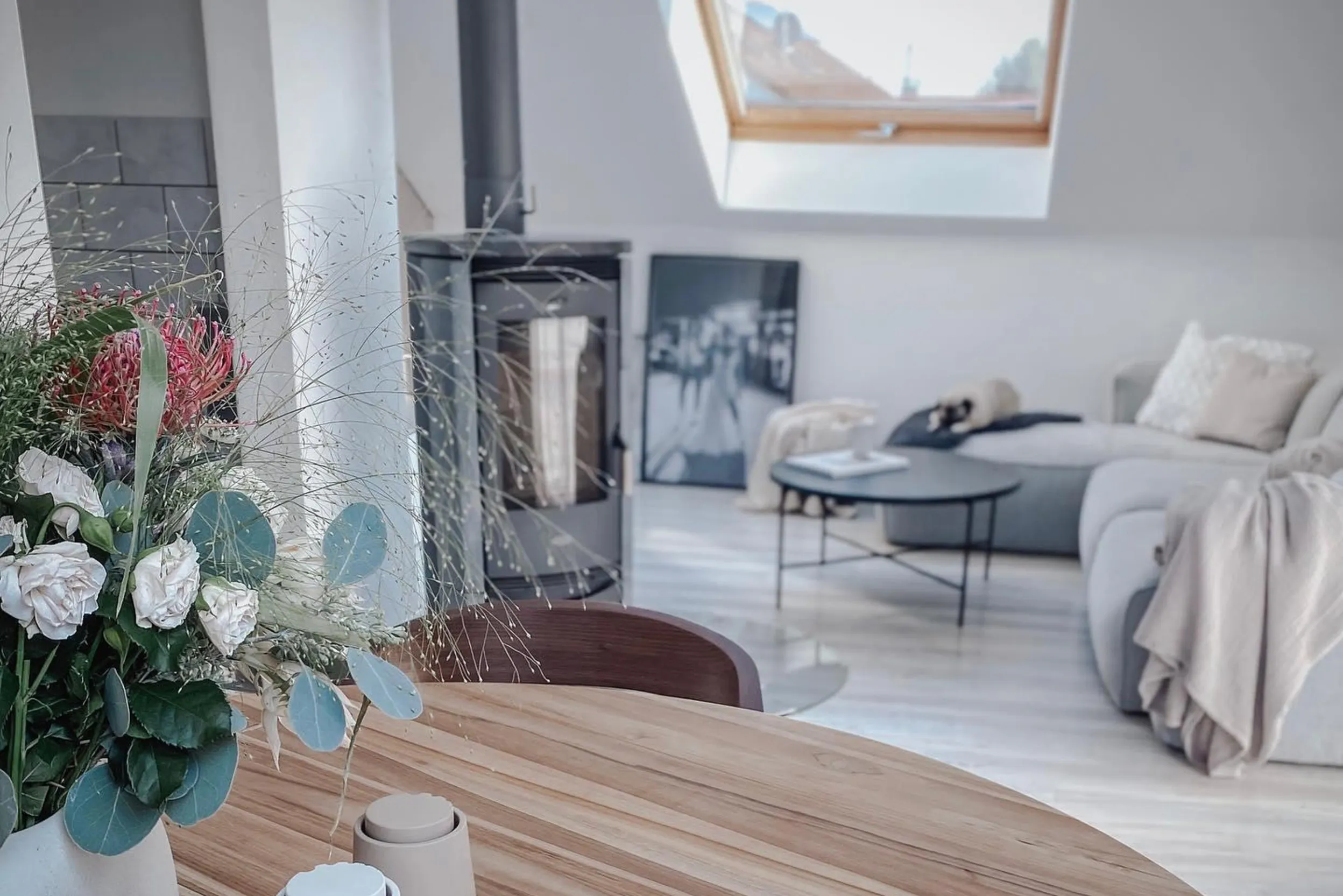 Im Vordergrund: runder Esstisch aus Holz, im Hintergrund: Sofaecke mit Eckcouch und Kamin