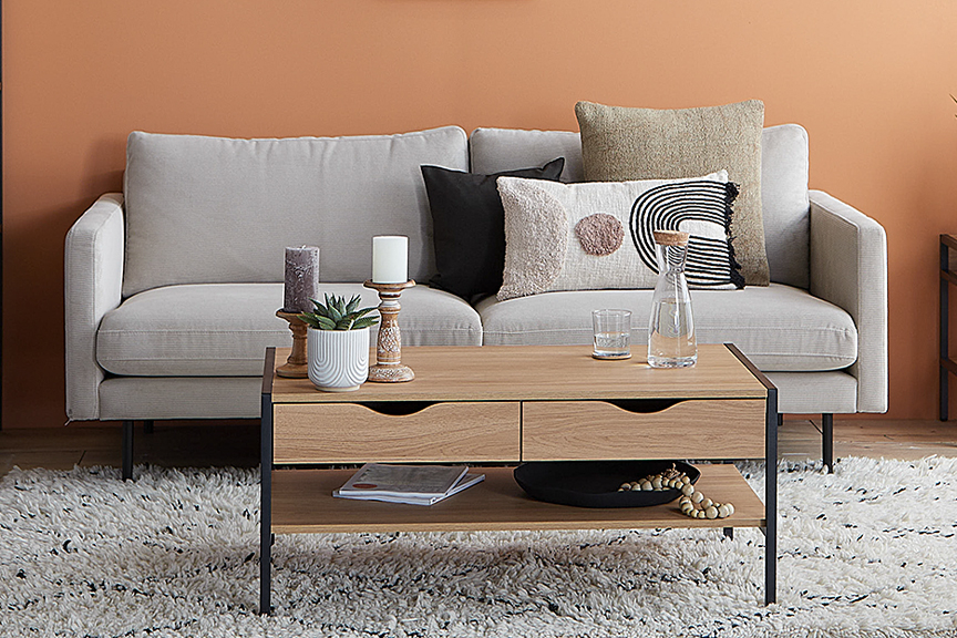 Wohnzimmer in Erdfarben mit einer Wand in sattem Terrakotta, davor ein beiges Cordsofa der Serie Landos und Möbel der Serie Mica der home24 Exklusivmarke Mørteens, dazu Deko aus Keramik von BUTLERS, ein cremefarbener Hochflorteppich sowie Wandbilder mit abstrakten Naturmotiven