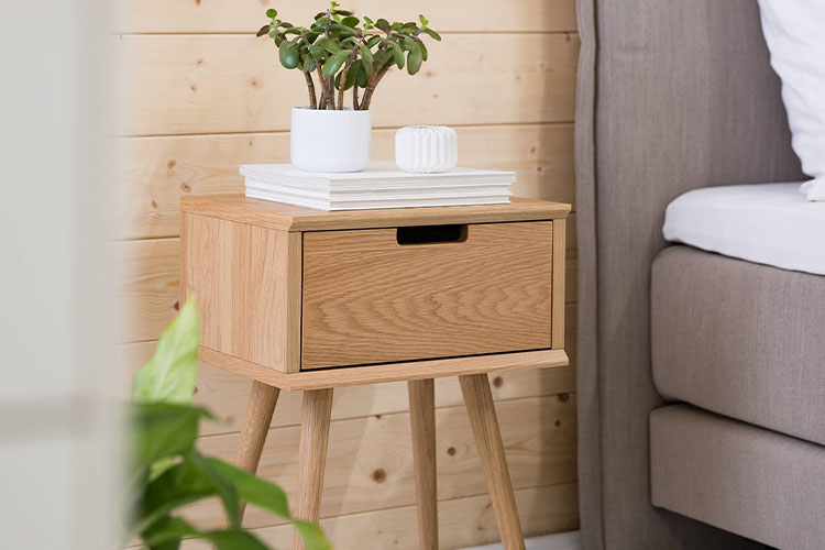 Nachttisch aus Holz mit ausgestellten Beinen im Skandi-Look vor einer Holzvertäfelung