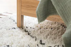 Detailbild eines Hochflorteppichs mit weiß-schwarzem Muster unter einem Bett