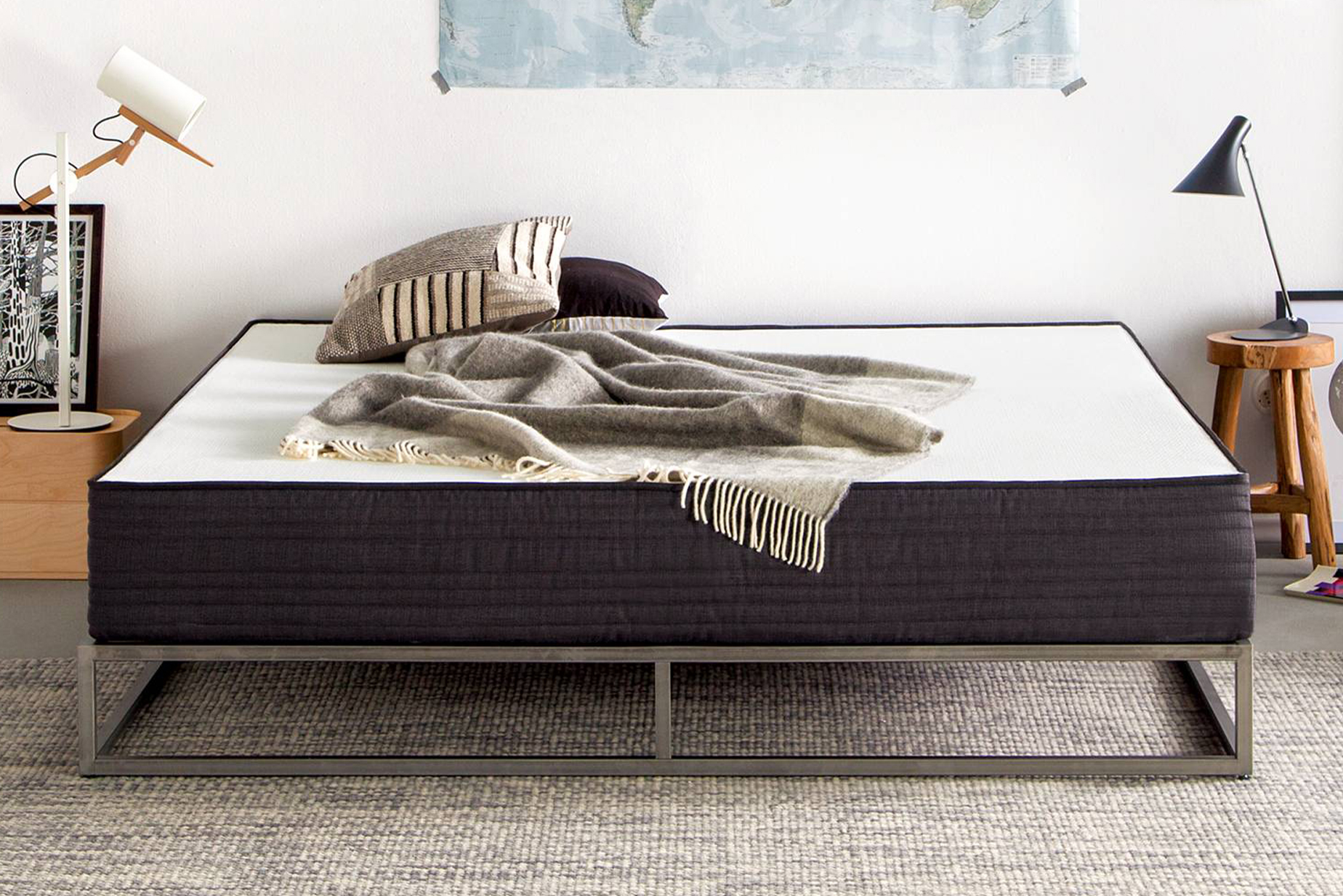 Dunkelblaue Matratze Smood mit weißer Liegefläche sowie beigen Kissen und einem beige kariertem Plaid auf einem Metallbett