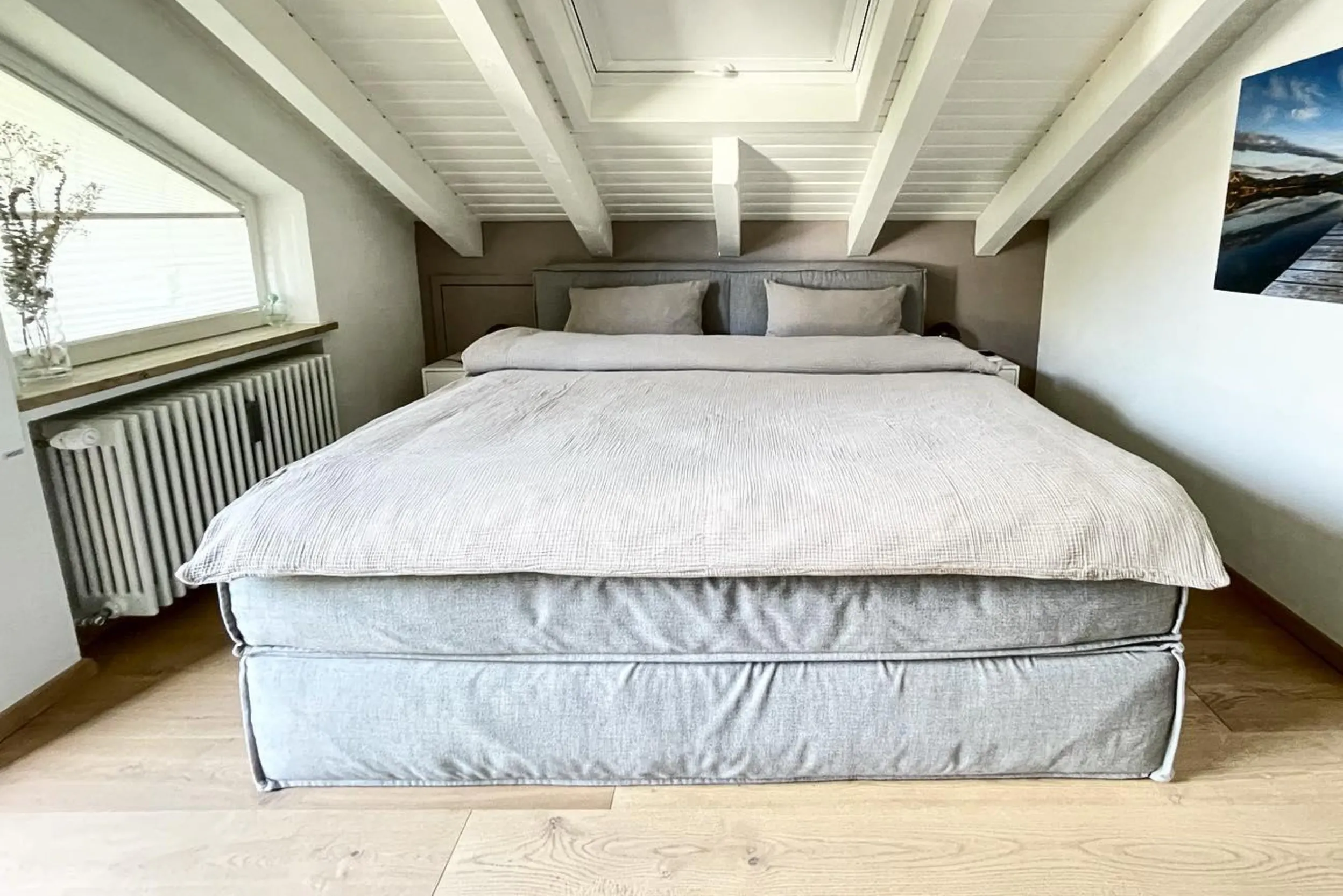 Graues Polsterbett unter einer Dachschräge mit Dachfenster