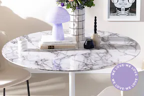 Runder Esstisch mit weißer Marmorplatte, beigen Polsterstühlen sowie farblich passender Deko wie einer schwarz-weißen Vase mit Frühlingsstrauß, lila Tischlampe im Mushroom-Look und schwarz-weißen Wandbildern.