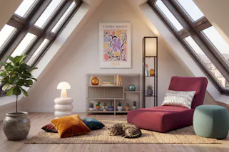 Weinroter Schlafsessel aus Cord mit silbernem und bunten Kissen, dazu Regale, ein Pouf sowie ein weißer Beistelltisch mit einer weißen Mushroom-Lampe.