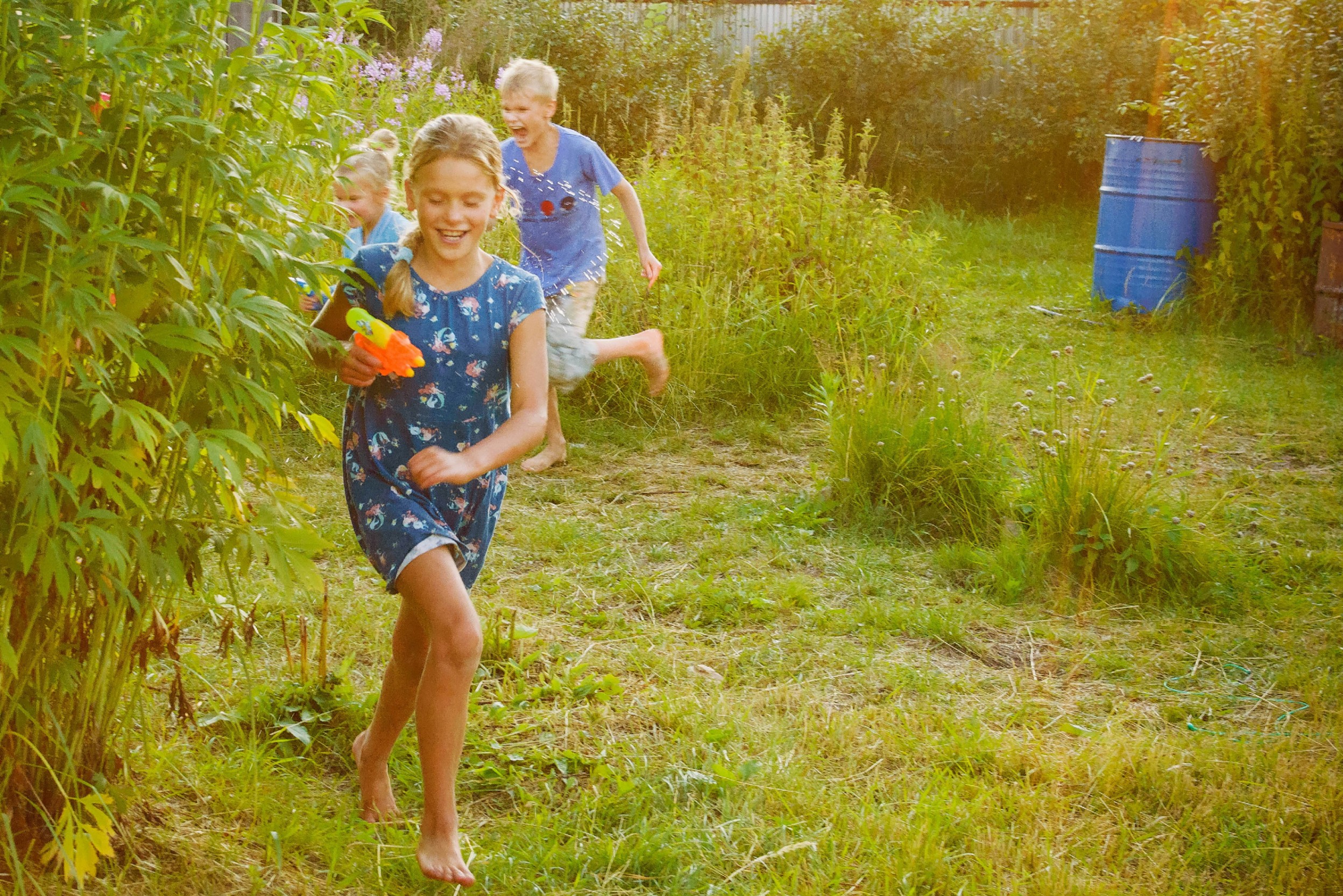Drei Kinder beim Spielen mit Wasserpistolen im Garten