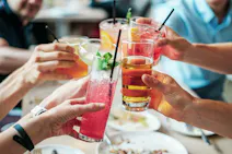 Plusieurs mains tenant des verres avec des boissons colorées et rafraîchissantes trinquant au-dessus d'une table avec des assiettes