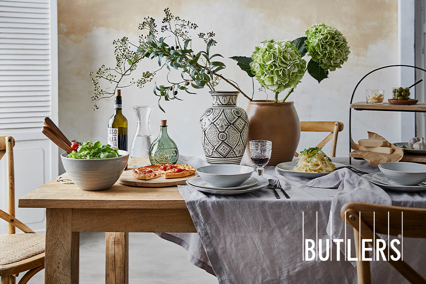 Mit Leinendecke gedeckter Holztisch, auf dem große Keramikvasen im toskanischen Stil drapiert sind und es von Pasta Toscana bis hin zu Pizza, Salat und Rotwein wohl keine italienische Köstlichkeit fehlt
