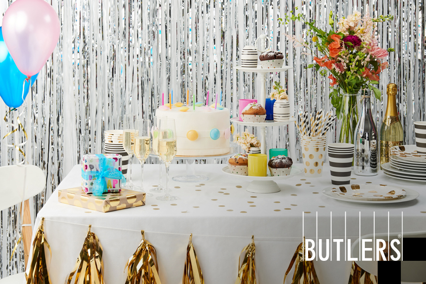Feierlich gedeckter Partytisch mit goldenem Konfetti, pastelligen Luftballons, Torte, Geschenken, Etagere, Sekt und mehr von BUTLERS.
