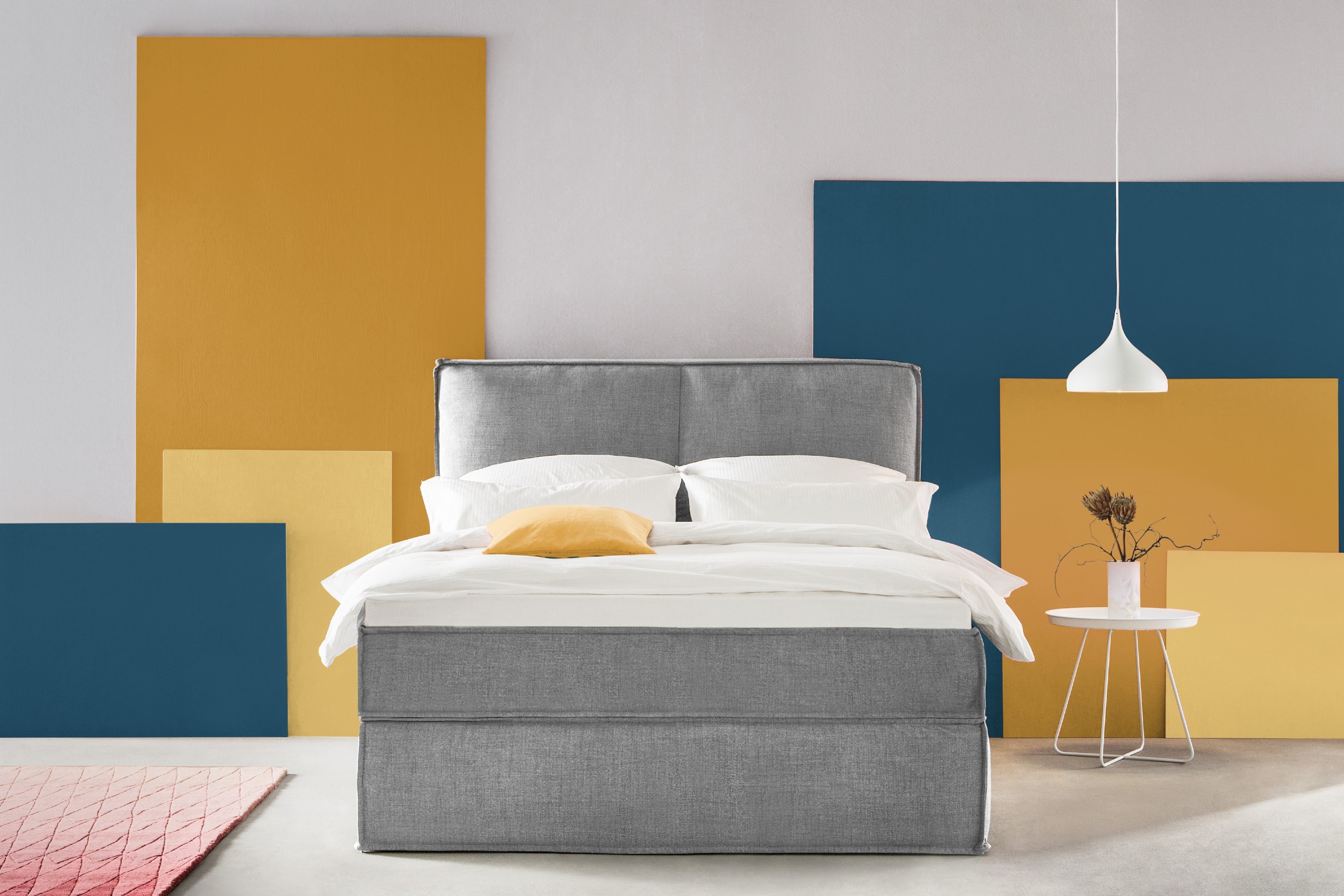 Graues Polsterbett vor Wand in Gelb und Blau