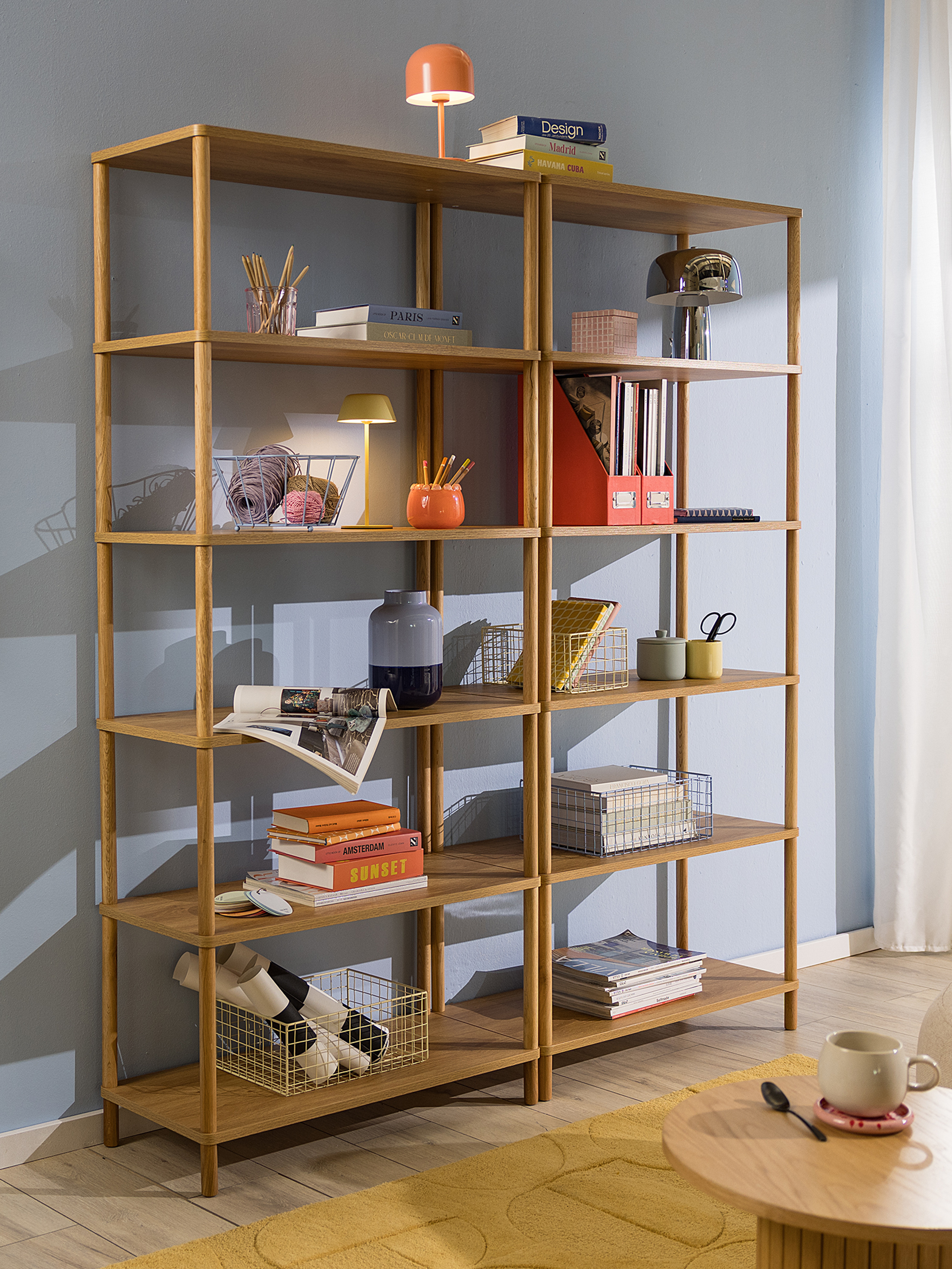 Modernes Standregal aus Holz vor himmelblauer Wand, dekoriert mit Körben, Büchern und Deko, dazu ein Holzregal mit Büchern und Schreibartikeln.