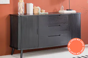 Sideboard aus schwarz lackiertem Eichenholz mit Schubkästen und seitlichen, geriffelten Schiebetüren vor einer roten Statement-Wand.