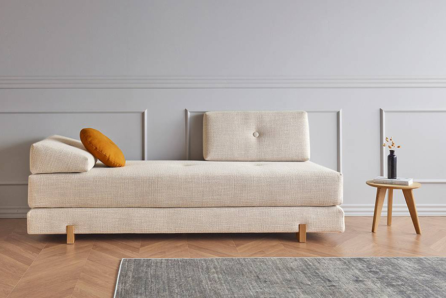 Beiges Schlafsofa mit Holzbeinen und senfgelbem Kissen in einer Altbauwohnung.