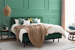 Grünes Bett vor grüner Wand mit Accessoires in Braun, Weiß und Grün