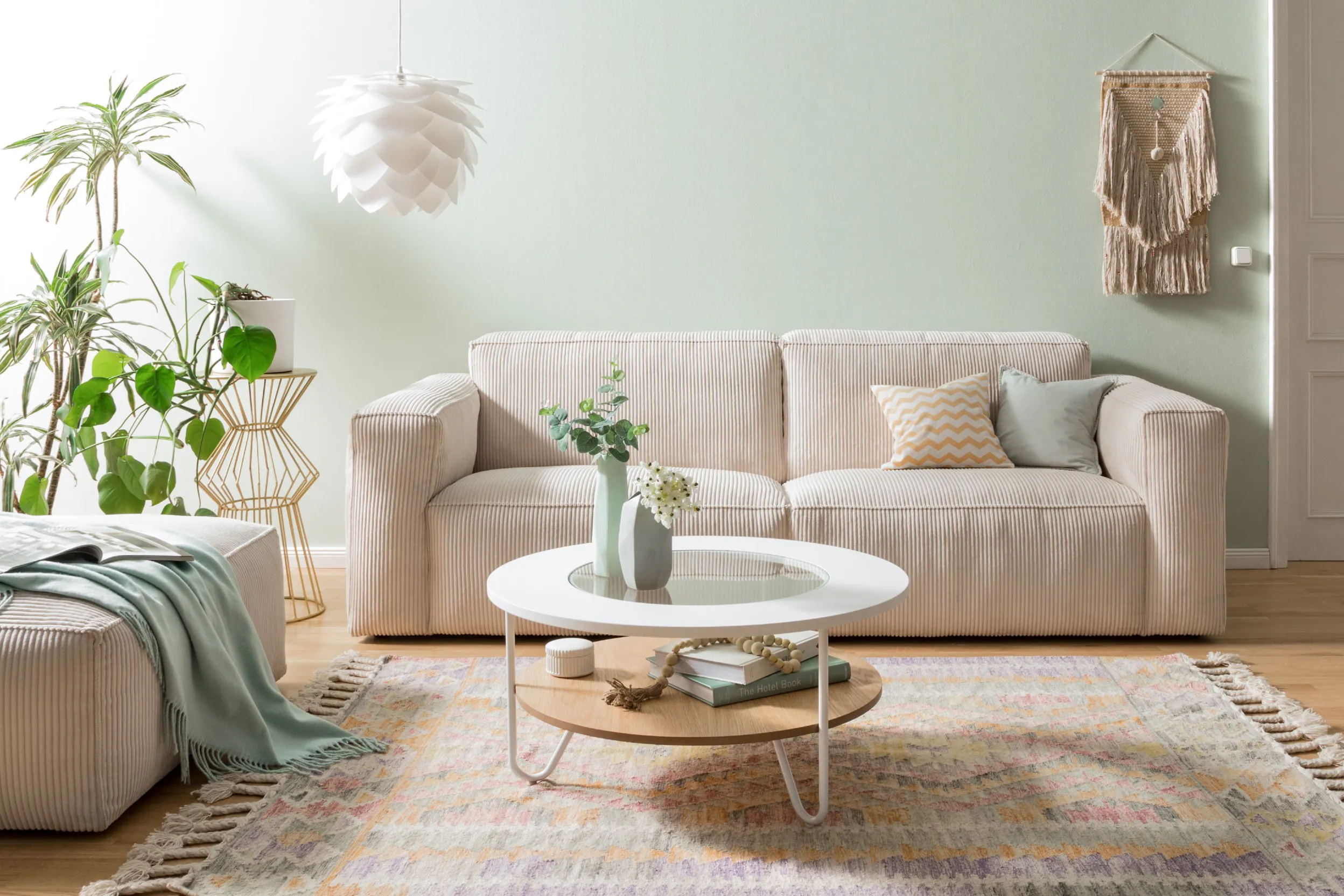 Beiges Cordsofa vor hellgrüner Wand in einem Wohnzimmer mit weißen und grünen Accessoires