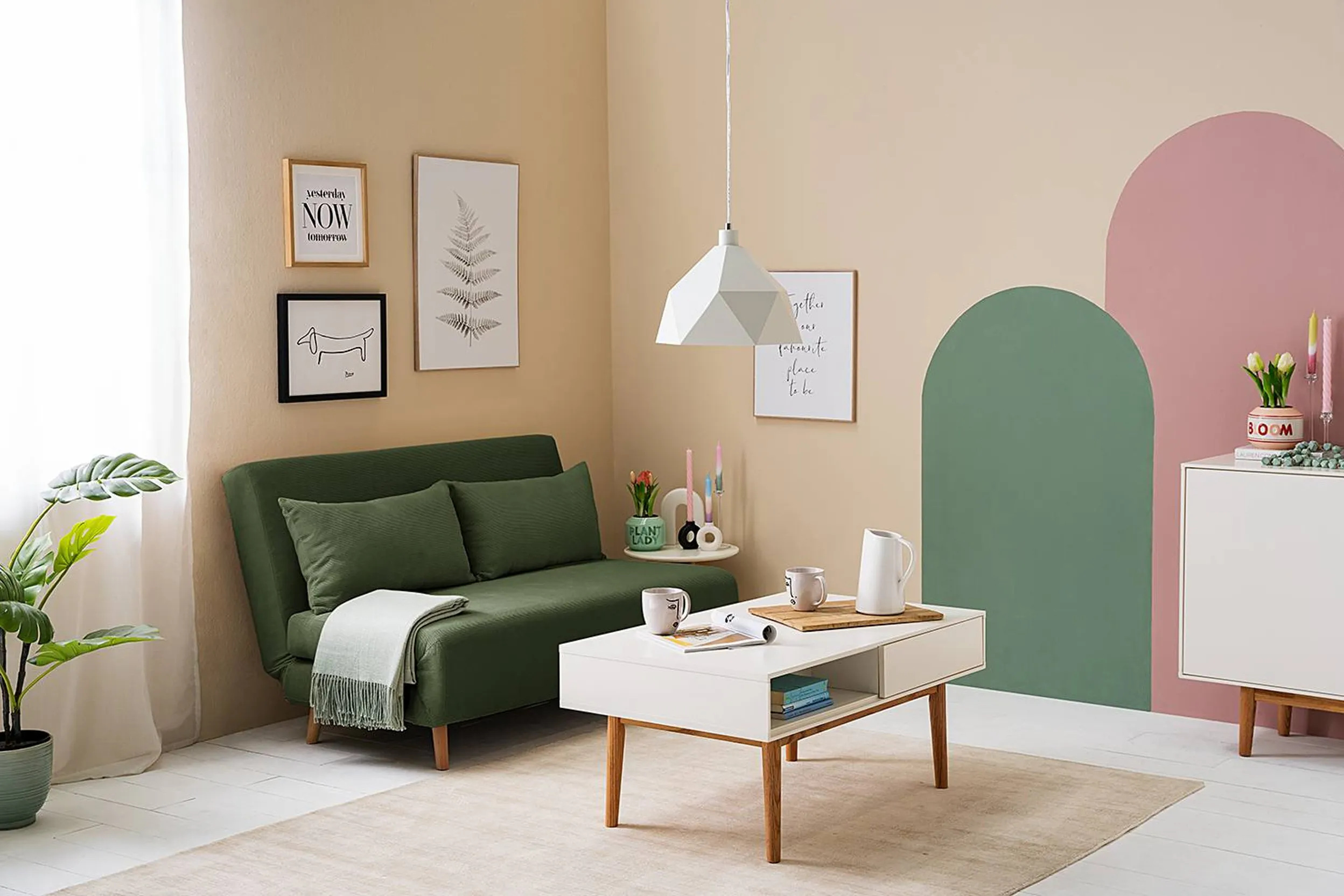 Grünes Schlafsofa kombiniert mit weißen Möbeln, cremefarbenen Wänden und rosa Akzenten