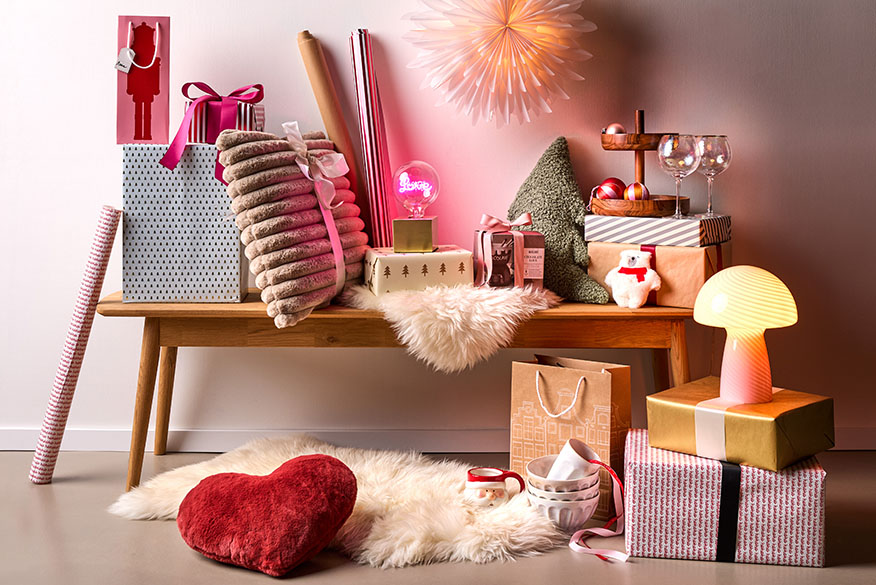 Différents cadeaux, lampes, coussins et autres articles dans des tons beiges et roses comme inspiration pour des idées de cadeaux de Noël.