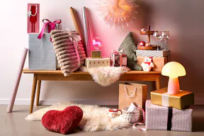 Différents cadeaux, lampes, coussins et autres articles dans des tons beiges et roses comme inspiration pour des idées de cadeaux de Noël.