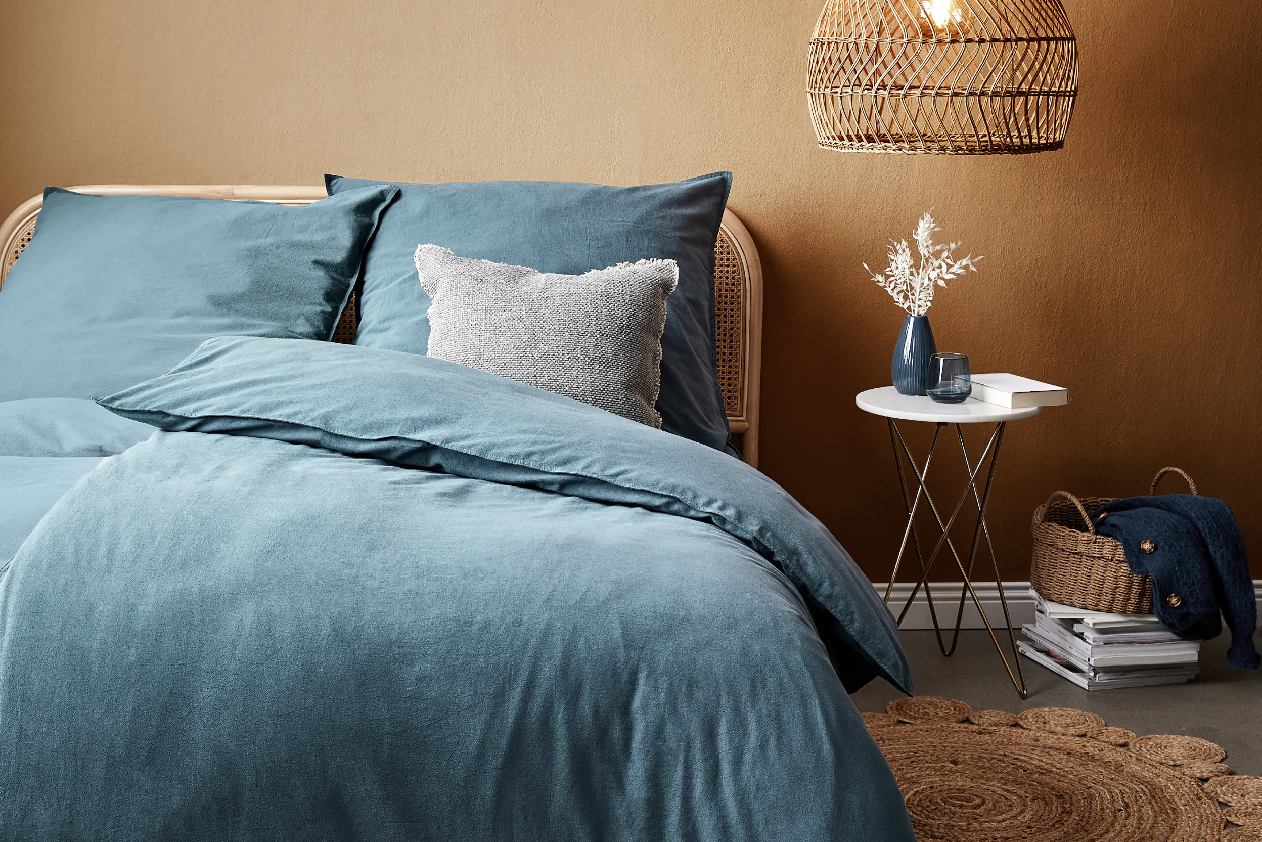 Rattanbett mit blauer Bettwäsche vor brauer Wand