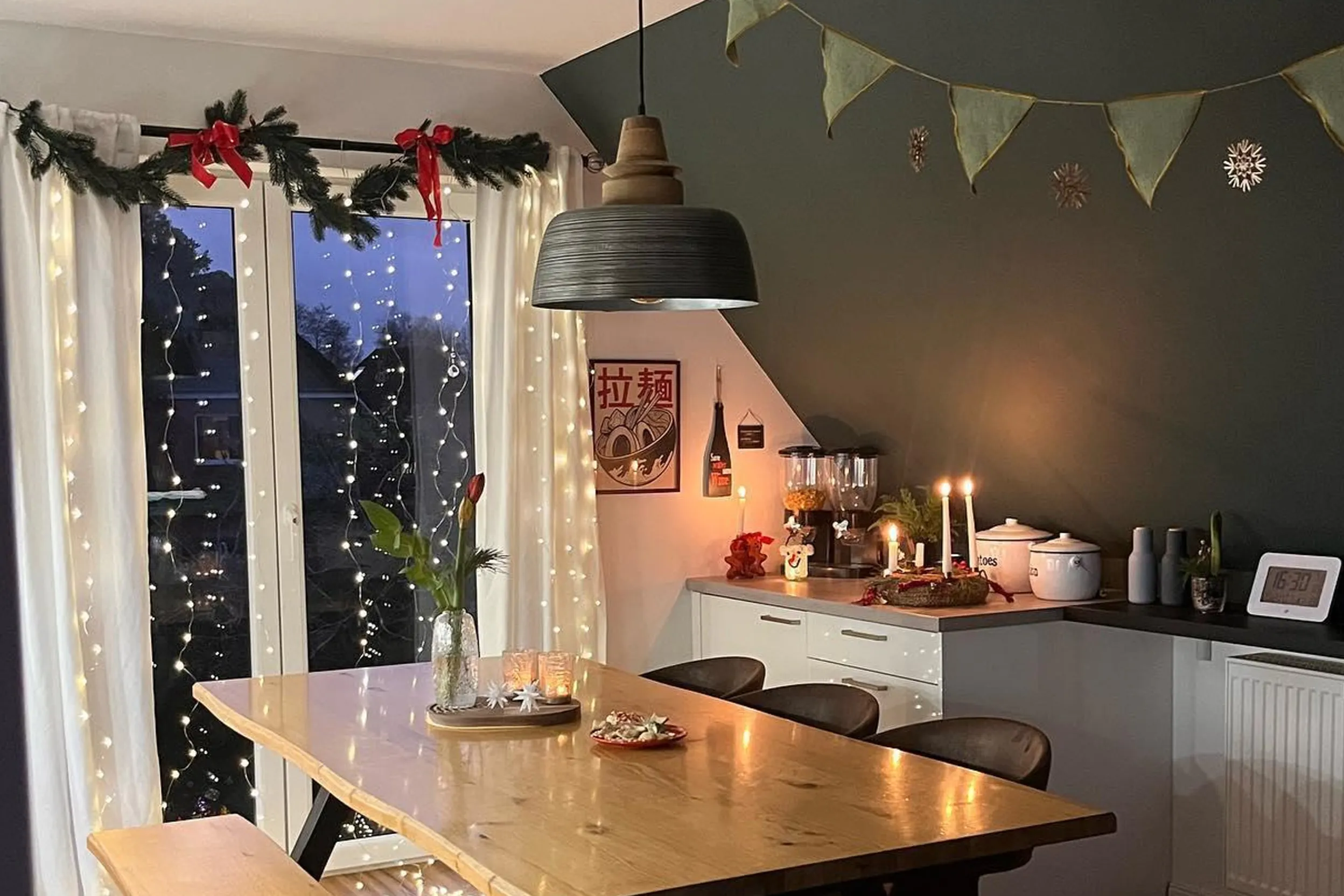 Weihnachtlich geschmücktes Fenster mit Tannen, Schleifen und Lichterketten in einer Küche