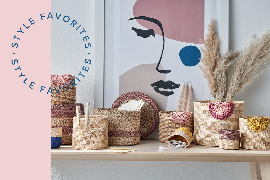 Körbe in verschiedenen Größen im Natur-Look und dunkelblauem bzw. rosafarbenem Muster; dieselbe Farbgebung wiederholt sich in der Illustration im Hintergrund sowie daneben im kleinen Detailbild, welches Dekohäuser und ein Bild vor einer Tapete in Rosé zeigt. 