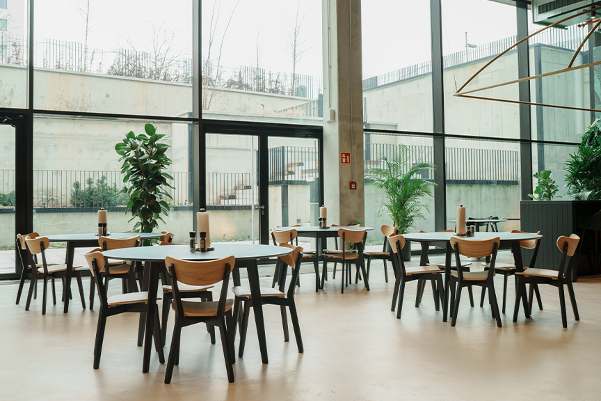 Mehrere Sitzgruppen aus Schwarz-Holz-Kombis im Industrial-Stil in einer Eventhalle vor großer Fensterfront