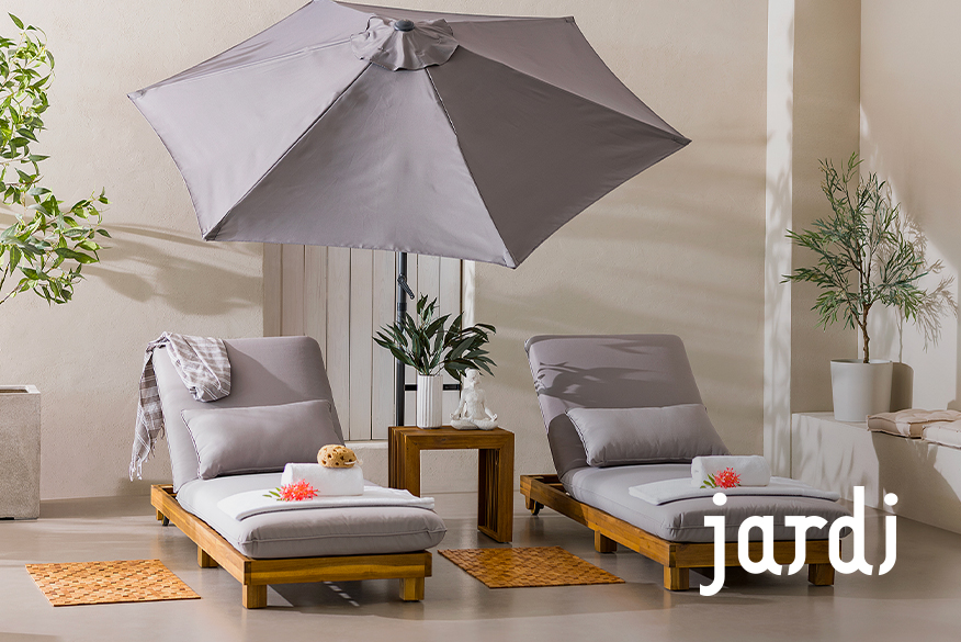 Zwei Sonnenliegen der home24 Exklusivmarke Jardi aus Massivholz mit hellgrauem Polster und passendem Kissen, die zum Relaxen auf der sonnigen Terrasse einladen.