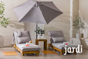Zwei Sonnenliegen der home24 Exklusivmarke Jardi aus Massivholz mit hellgrauem Polster und passendem Kissen, die zum Relaxen auf der sonnigen Terrasse einladen.