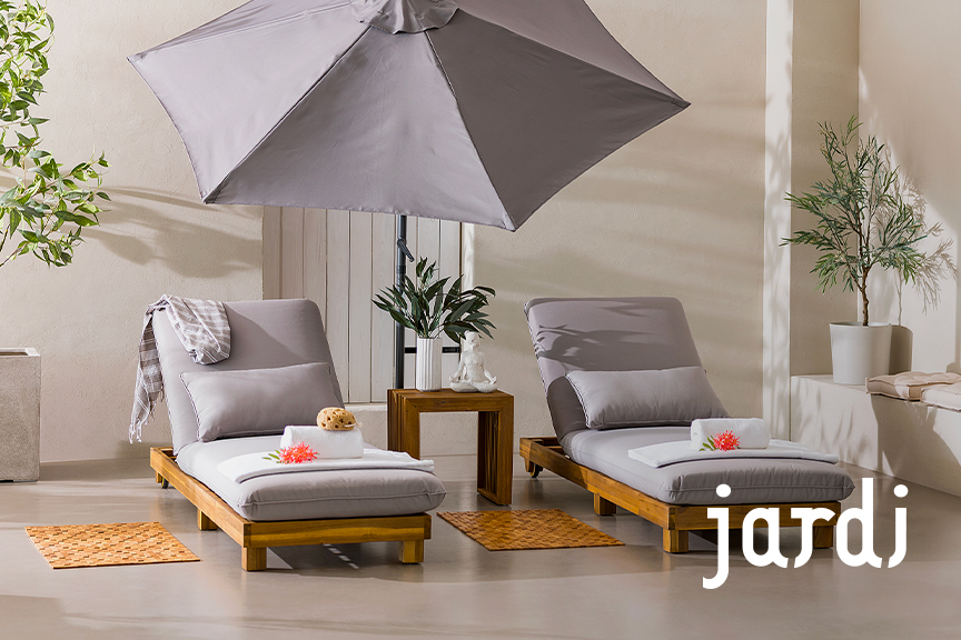 Zwei Sonnenliegen der home24 Exklusivmarke Jardi aus Massivholz mit hellgrauem Polster und passendem Kissen, die zum Relaxen auf der sonnigen Terrasse einladen.