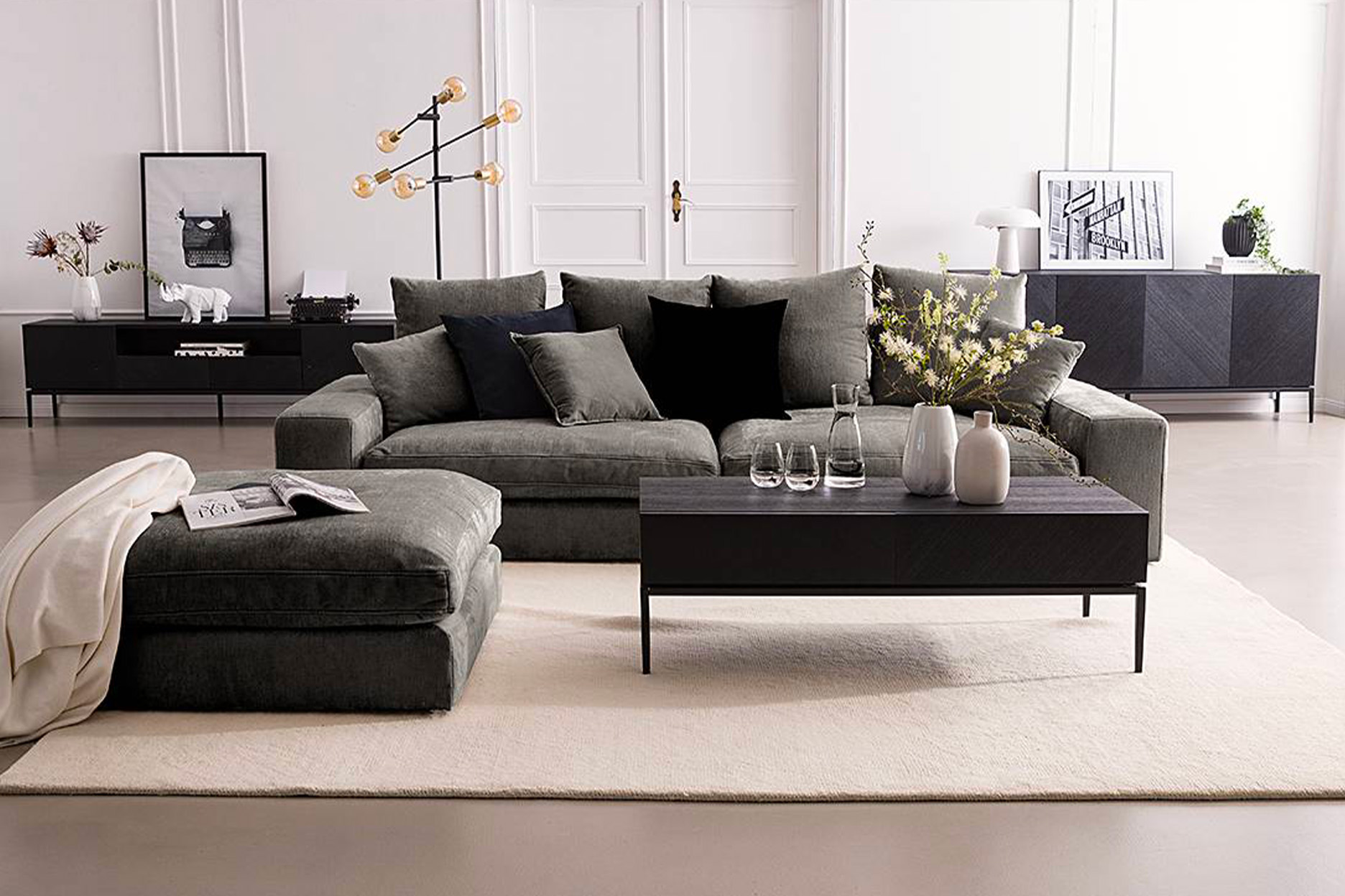 Salon moderne et élégant avec canapé d’angle gris, table basse noire décorée de vases, et buffet assorti dans un intérieur lumineux au style minimaliste.